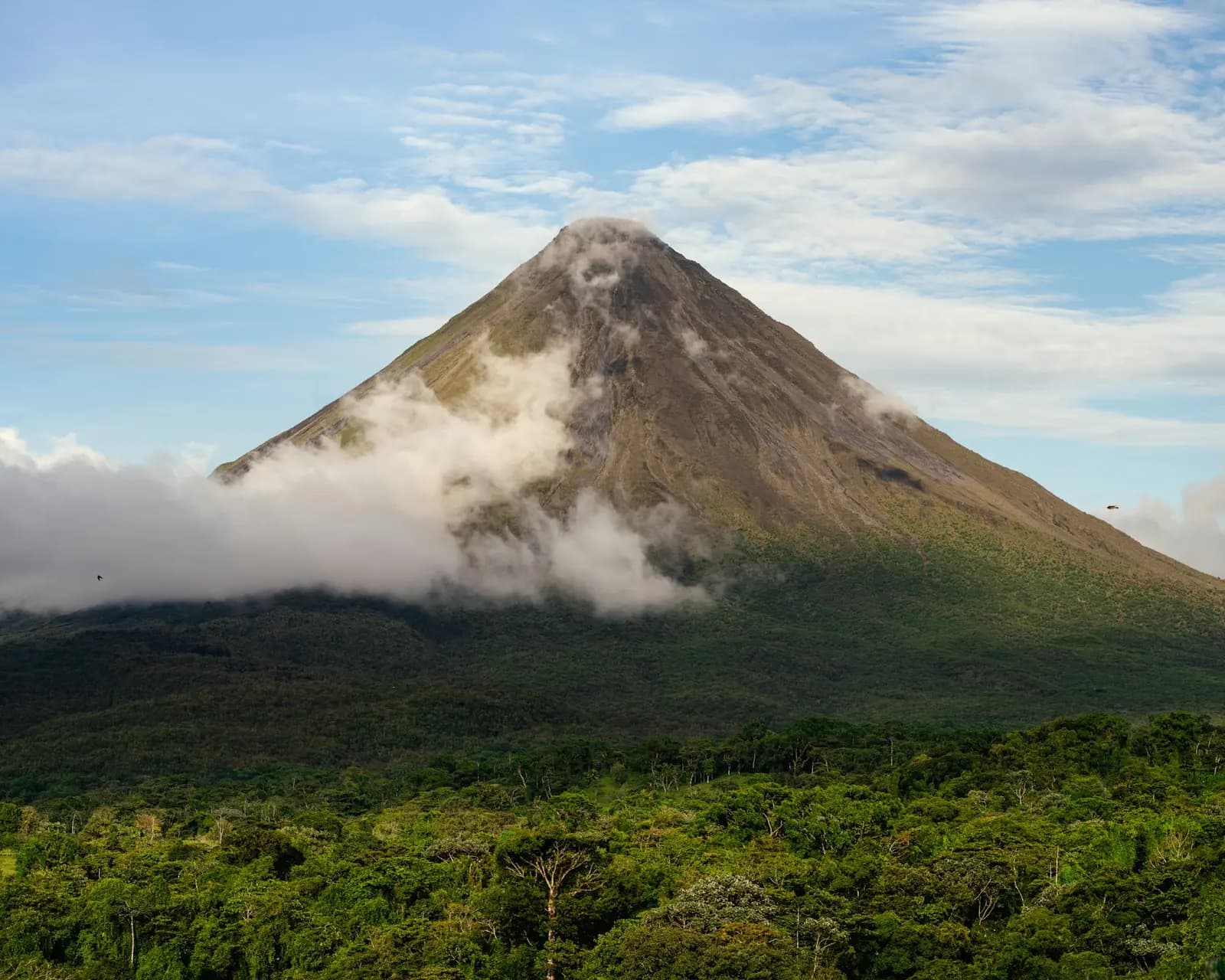Arenal Volcano rising above the rainforest with clouds around its base