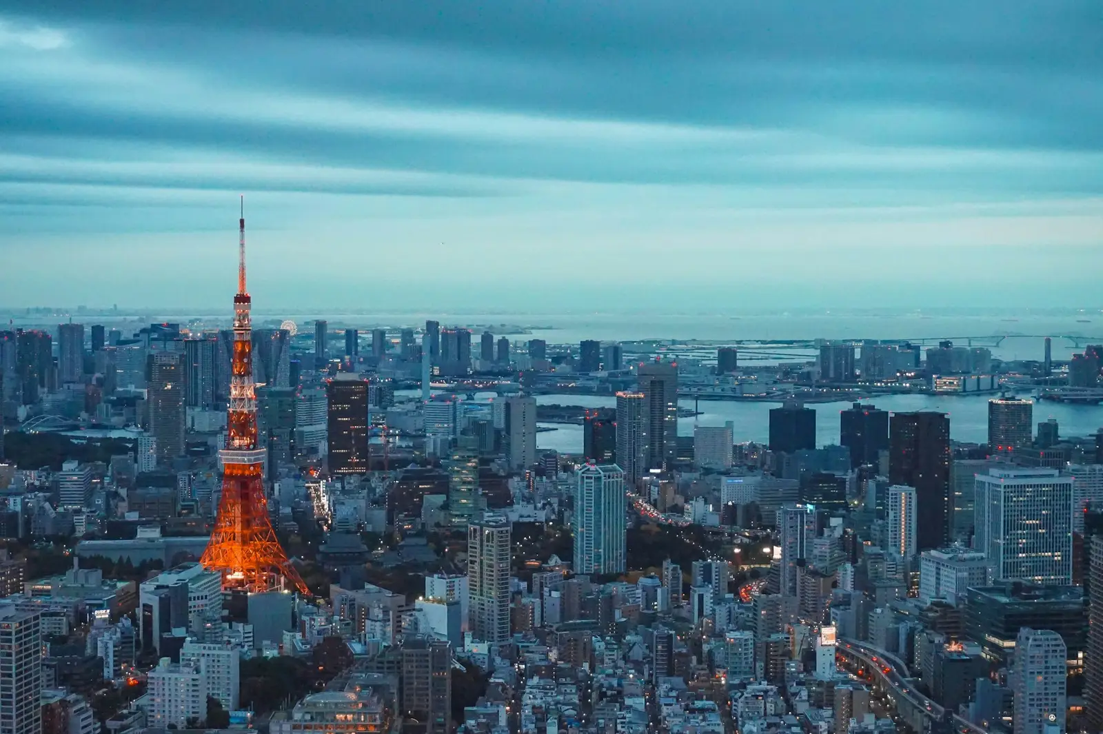 Tokyo Tower lit up at dusk above the city, with Tokyo Bay behind