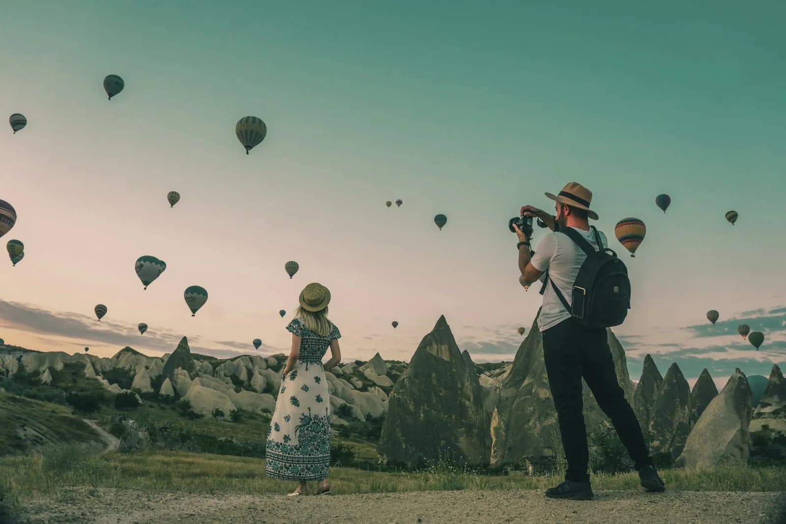 Dos viajeros mirando globos aerostáticos al amanecer