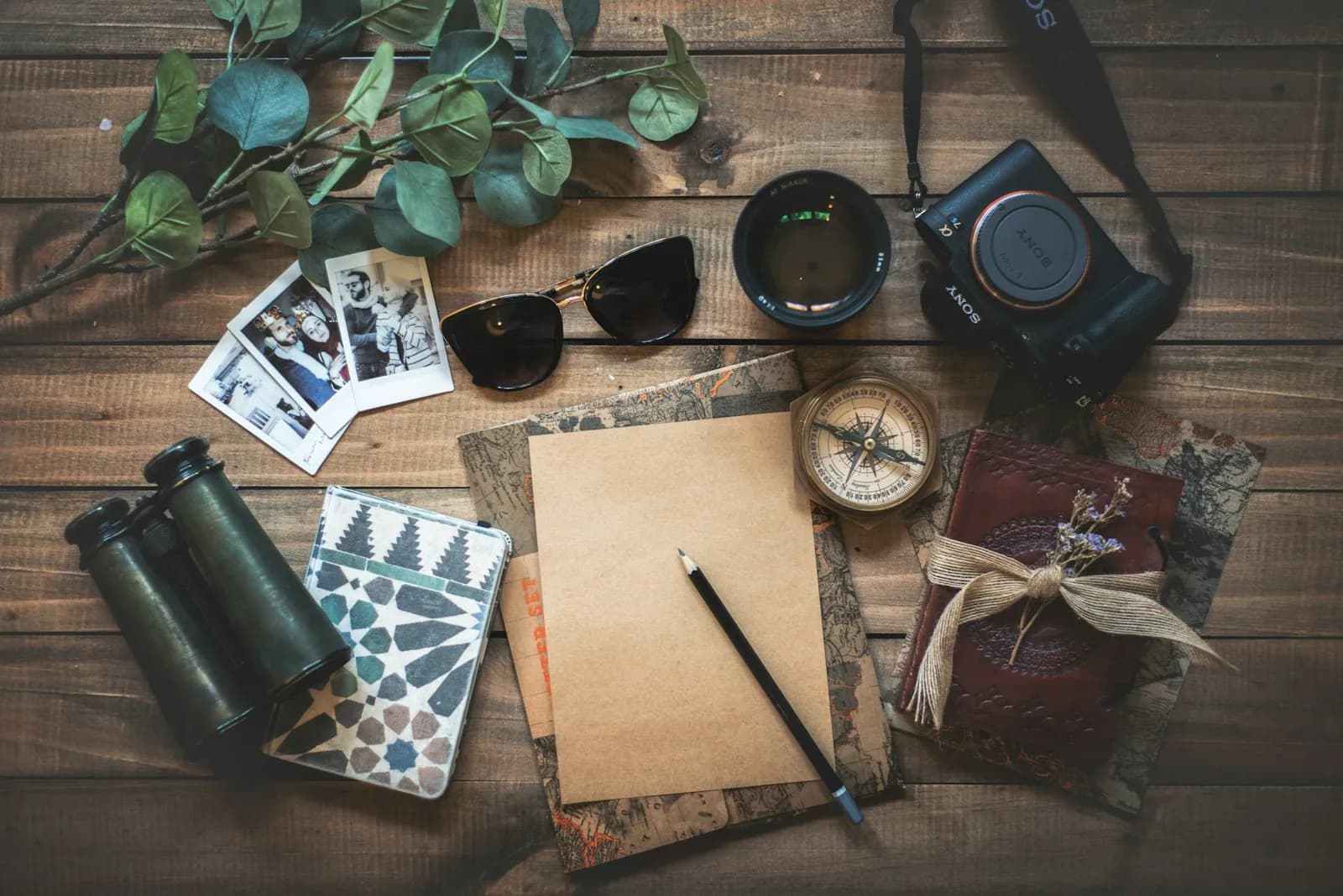 A camera, compass, notebook and instant photos on a wooden table