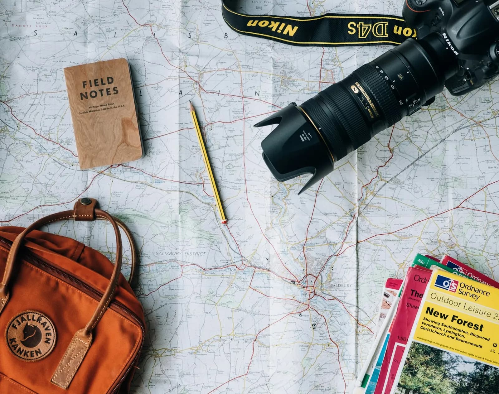 A paper map, notebook, camera and backpack laid out for a trip