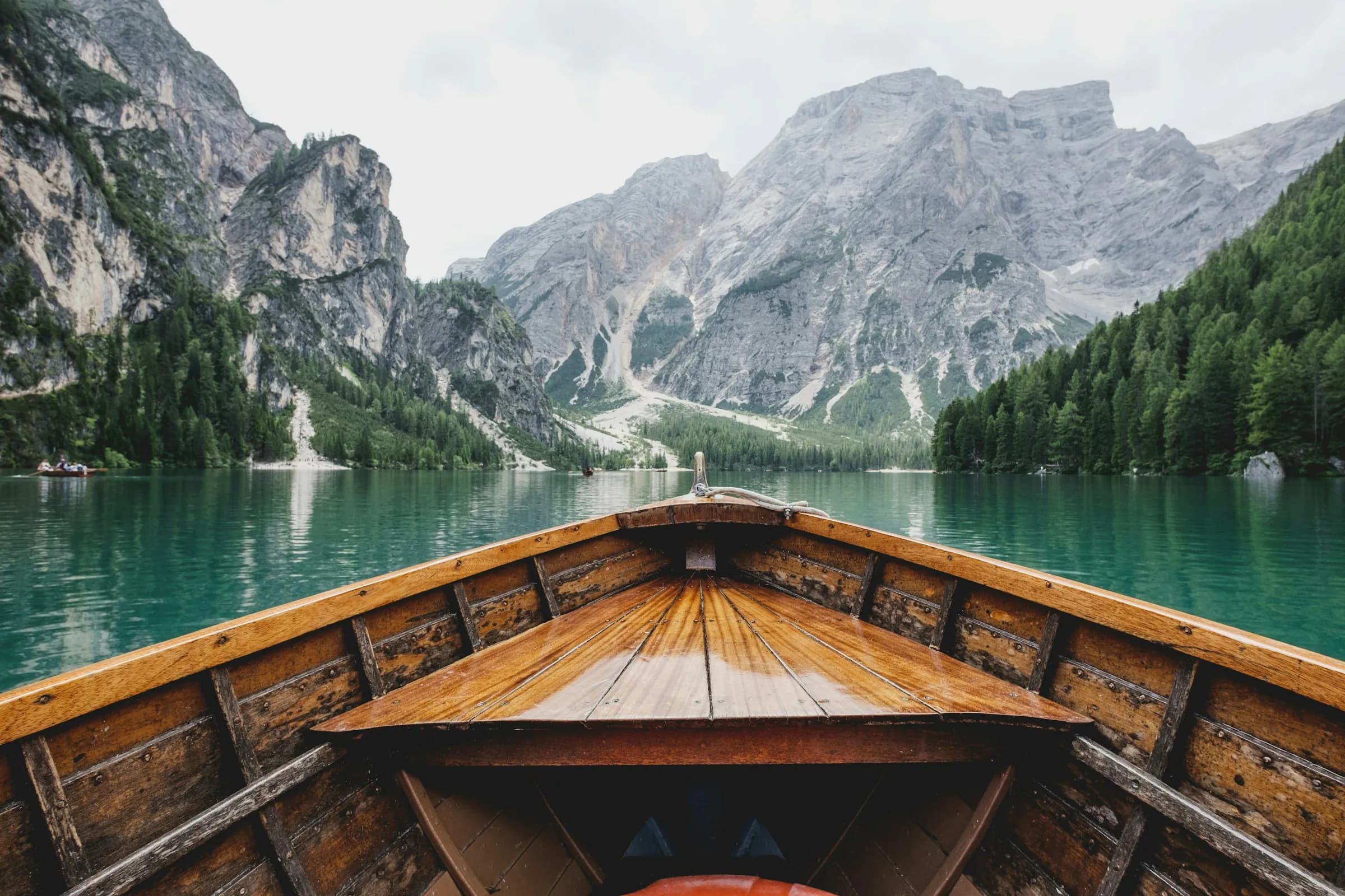 Vista desde la proa de un bote de madera sobre un lago entre montañas