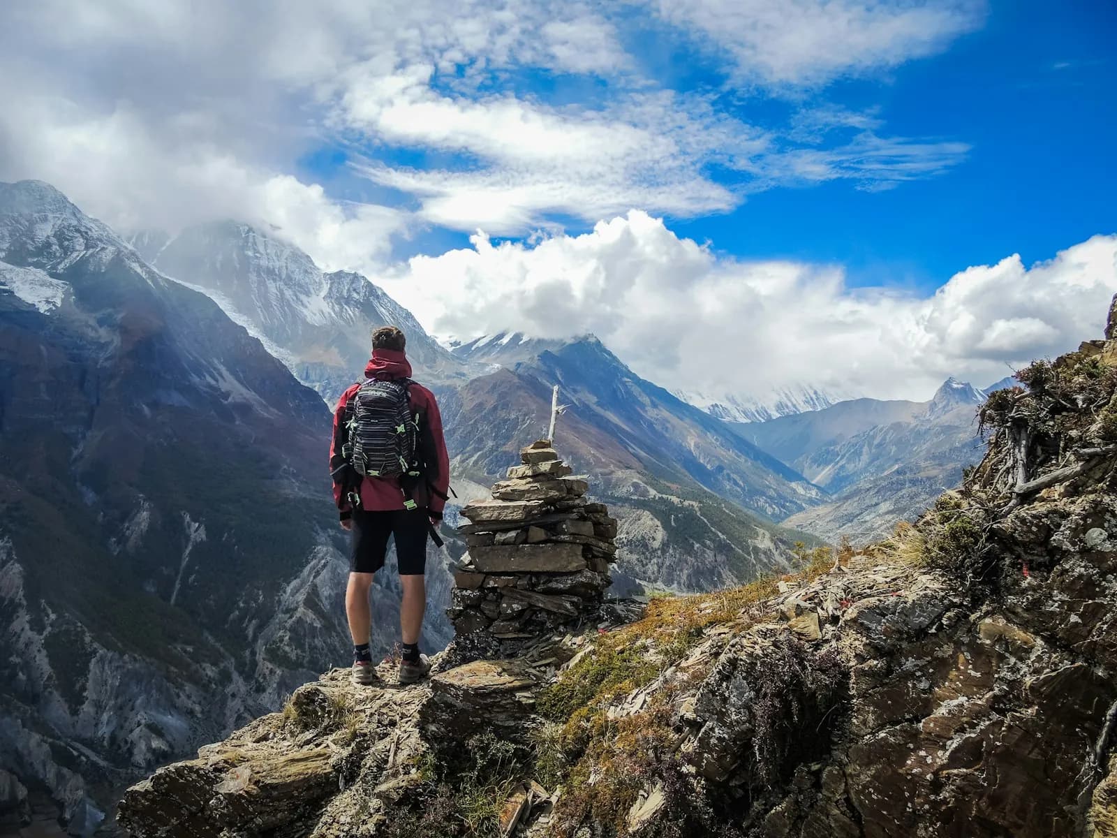 Un excursionista con mochila de pie en una cima rocosa sobre un valle entre montañas
