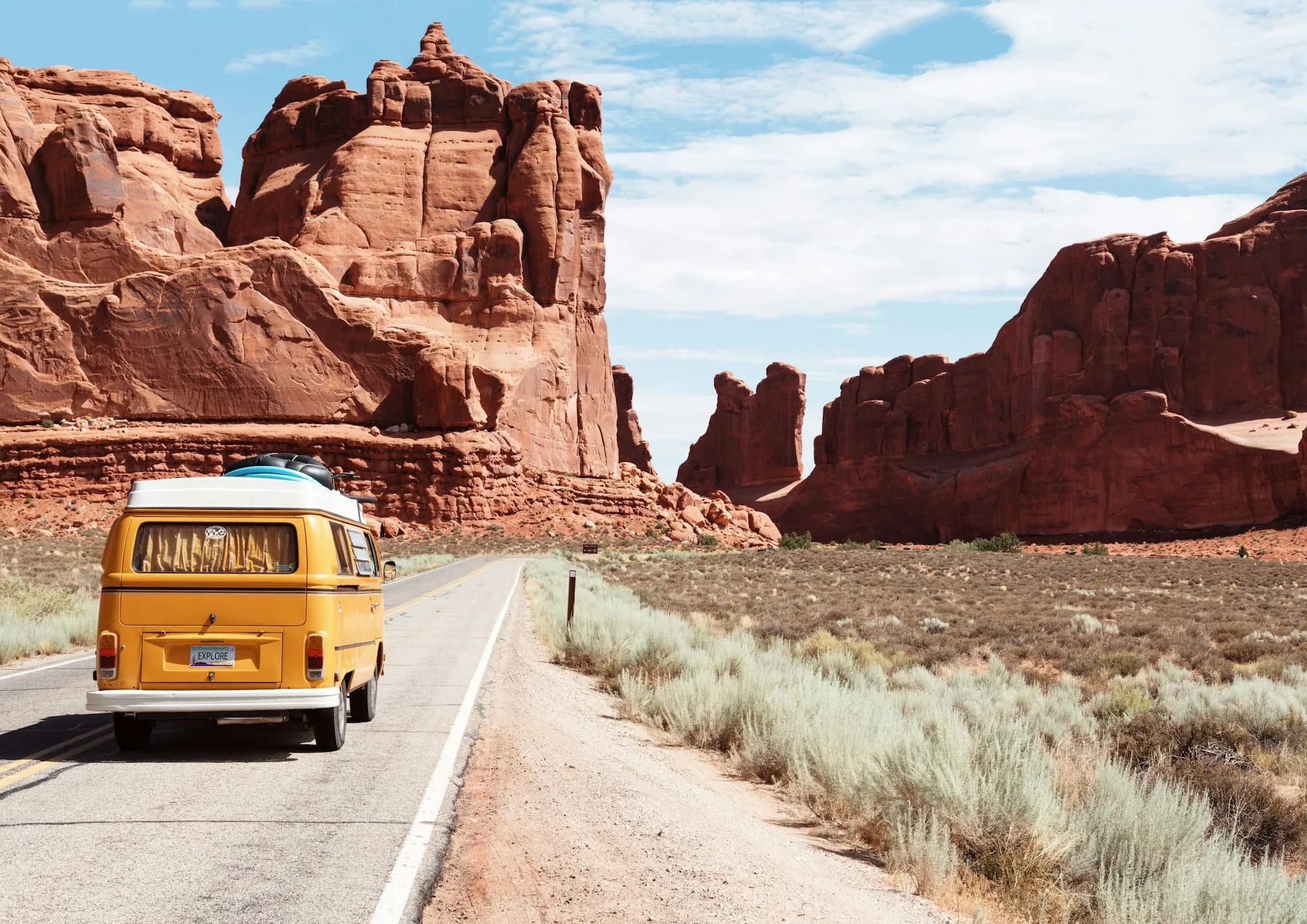A yellow camper van on a desert road between red rock cliffs